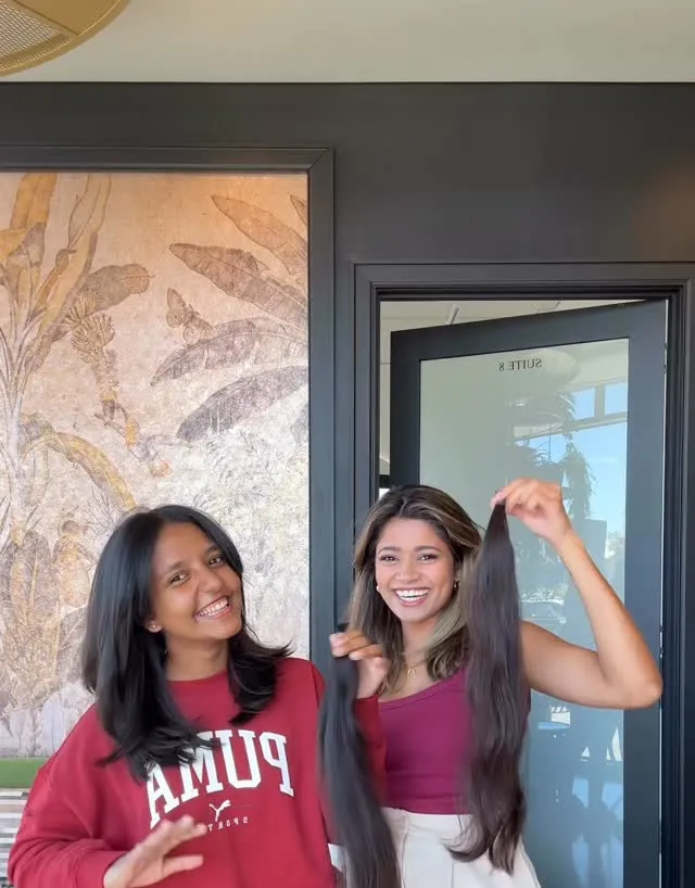 A client and her stylist smiling and holding up a long ponytail cut for donation