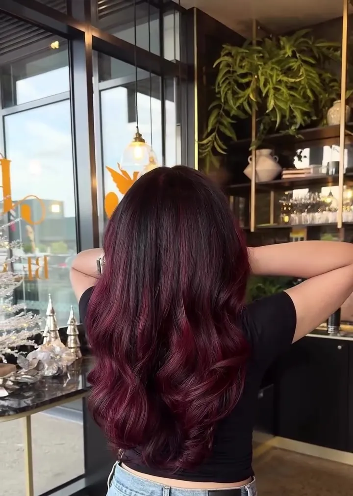 Long, curled cherry-red hair seen from behind, hands lifted to the head