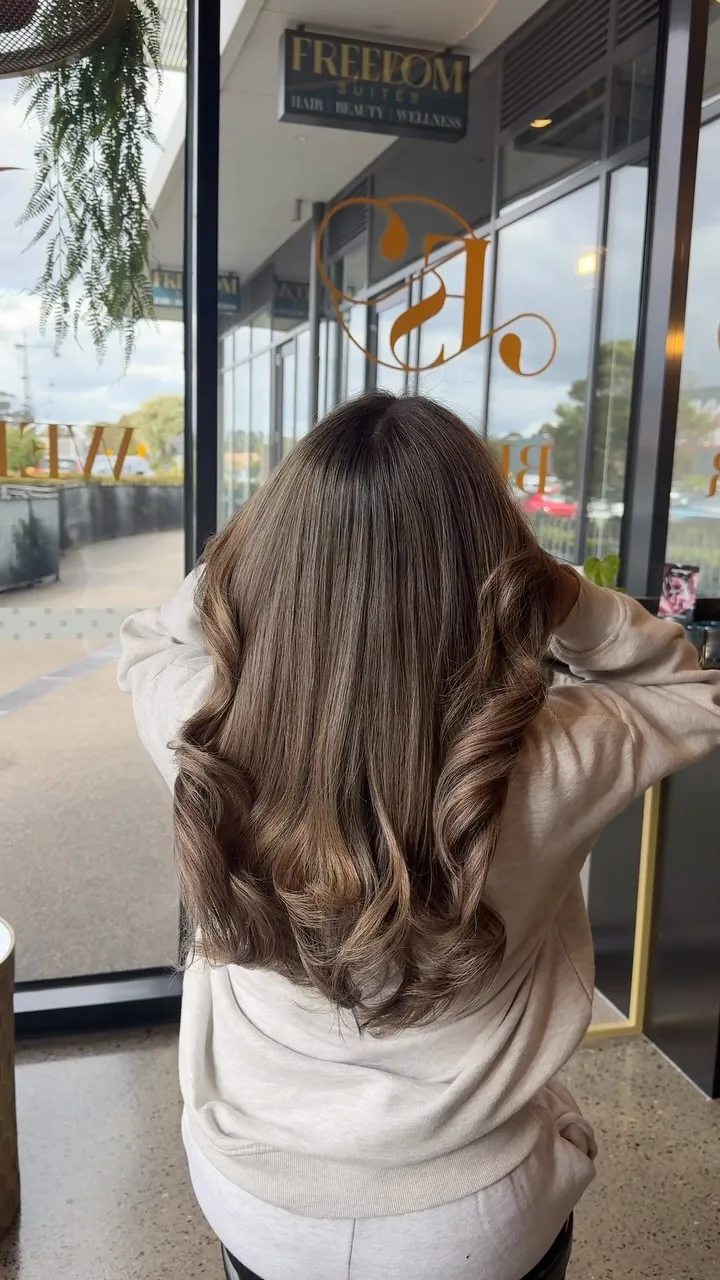Long brunette hair with soft blonde ribbons in loose waves, by a window in the salon