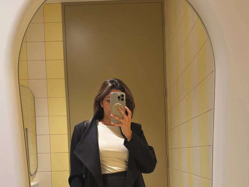 Oshi’s mirror selfie in a long black coat and white top, framed by an arched mirror