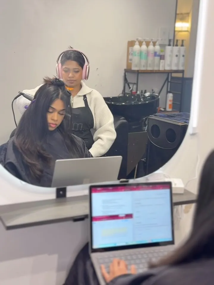 A quiet appointment: the stylist works with headphones on while the client types on her laptop